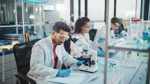 Medical Science Laboratory  Row of Diverse Team of Multi-Ethnic Young Scientists Looking Under Microscope  Analyze Chemicals  Talk  Solving Problems. Biotechnology Specialists working in Advanced Lab