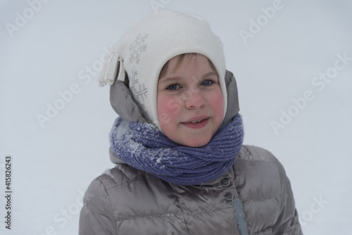 The child lies in deep snow and smiles sweetly. A beautiful girl in a snow-white environment. Concept for winter holidays and walks. Place for text