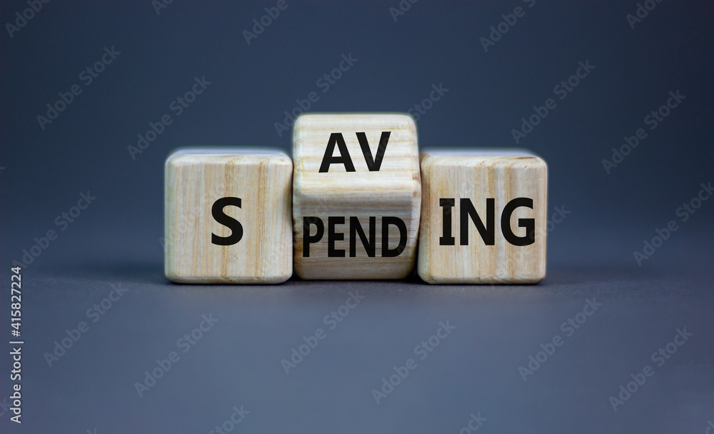Saving or spending symbol. Turned cubes and changed the word 'spending' to 'saving'. Beautiful grey table, grey background, copy space. Business and saving or spending concept. Saving or spending symbol. Turned cubes and changed the word 'spending' to 'saving'. Beautiful grey table, grey background, copy space. Business and saving or spending concept.