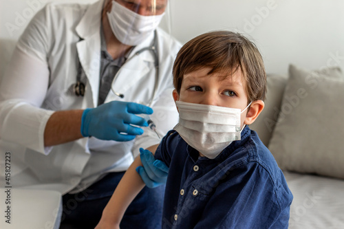 Selective focus of adorable little boy looking away  while male doctor holding a syringe and vaccinating him. A boy in a doctors office  looks concerned as he gets injected. Doctor vaccinating  boy.