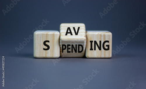 Saving or spending symbol. Turned cubes and changed the word 'spending' to 'saving'. Beautiful grey table, grey background, copy space. Business and saving or spending concept.