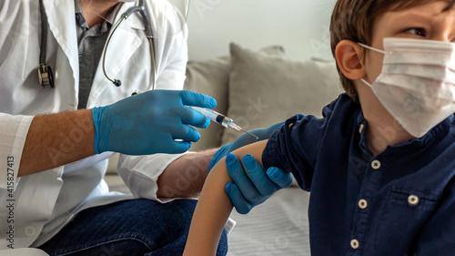Male pediatrician doctor or nurse with syringe making injection of vaccine for cute little boy patient at clinic or hospital. Selective focus of a pediatrician makes vaccination to cute Caucasian boy.