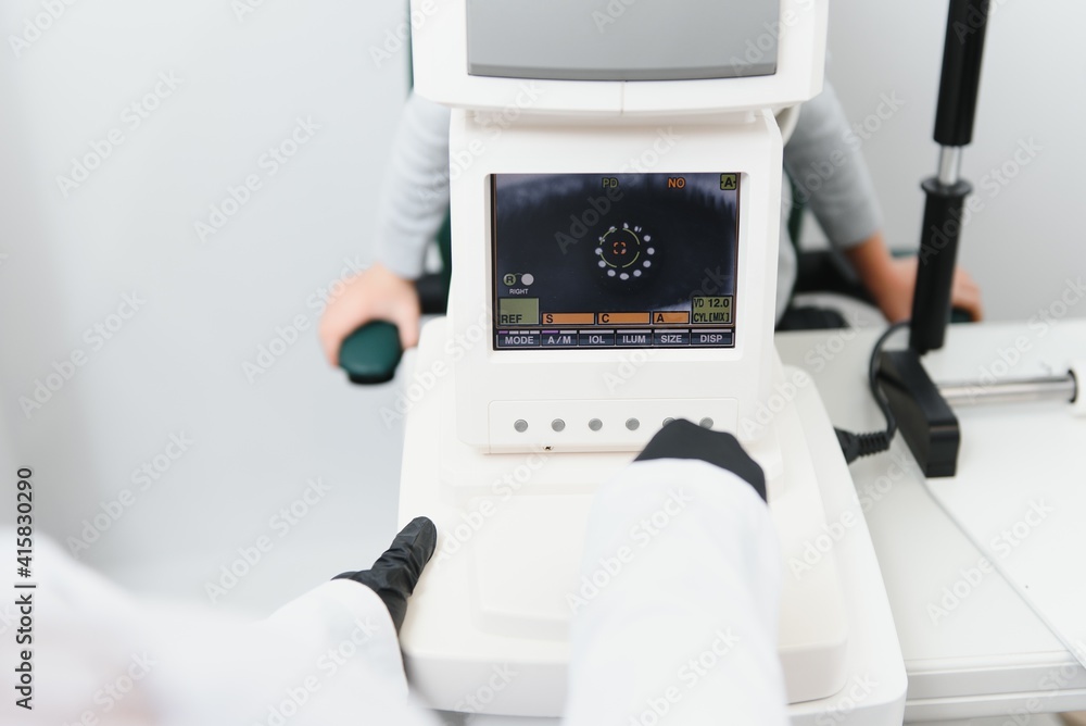 Modern medical equipment. Close up of ophthalmologist using auto refractometer while examining child eyes Modern medical equipment. Close up of ophthalmologist using auto refractometer while examining child eyes