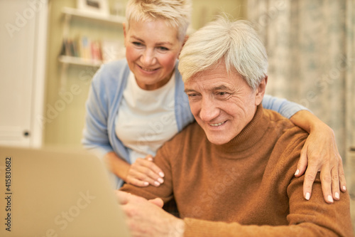 Cozy image of joyful blonde female and gray haired cheerful on retirement enjoying modern technology using generic laptop for video virtual call via application, speaking to grandchildren, smiling