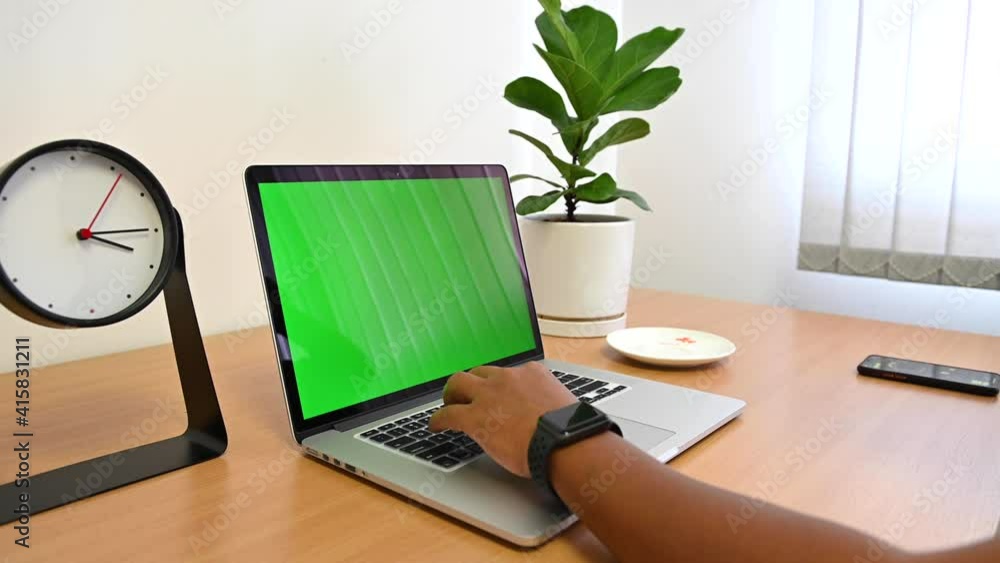 Person working with green screen of laptop computer with monstera plants and table clock on wooden table Person working with green screen of laptop computer with monstera plants and table clock on wooden table