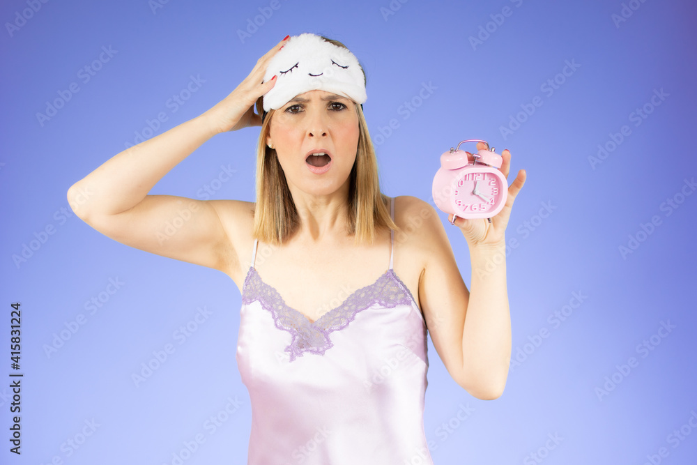 Young beautiful woman in nightgown holding a clock over purple background. Young beautiful woman in nightgown holding a clock over purple background.