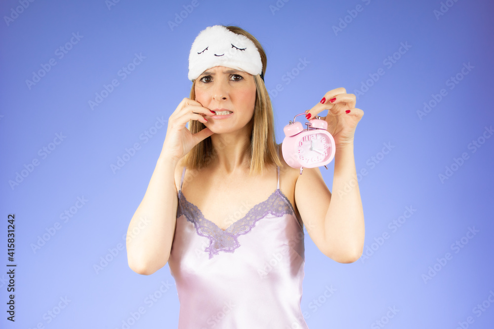 Young beautiful woman in nightgown holding a clock over purple background. Young beautiful woman in nightgown holding a clock over purple background.