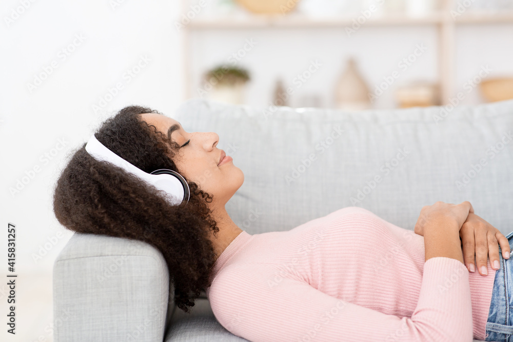 Happy calm young woman in earphones rest on cozy sofa, enjoy good quality sound Happy calm young woman in earphones rest on cozy sofa, enjoy good quality sound