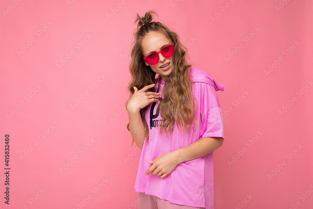 Charming sad young blonde curly woman isolated on pink background wall wearing casual pink t-shirt and stylish colourful sunglasses looking at camera and asking Charming sad young blonde curly woman isolated on pink background wall wearing casual pink t-shirt and stylish colourful sunglasses looking at camera and asking