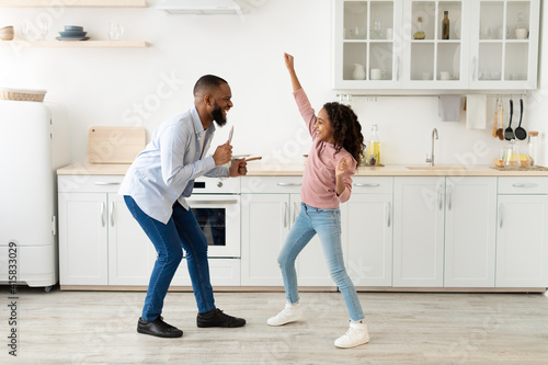 Black father and daughter dancing in the kitchen together © Prostock-studio