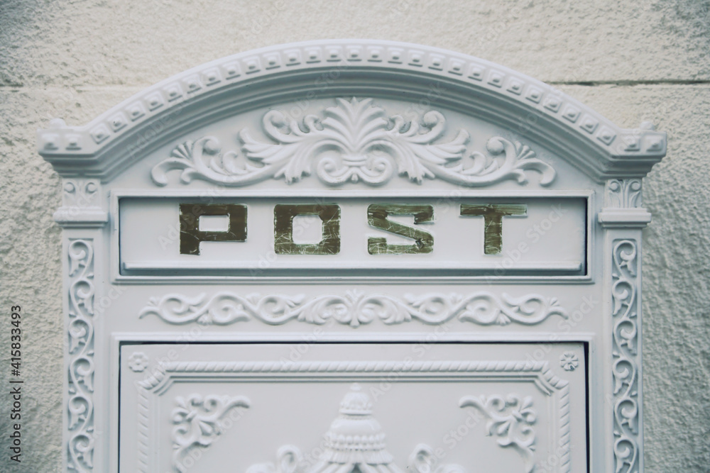 The elegant white slot of a luxury mailbox, with the word Post. Isolated on a creamy white wall surface.
