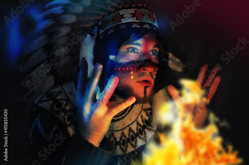 Portrait of a young handsome guy in a hat with a feather of the chief of the Indians. Fire and man - portrait
