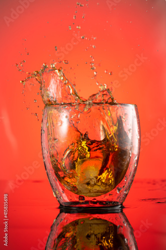 splash in a glass of whiskey from falling ice on a red background