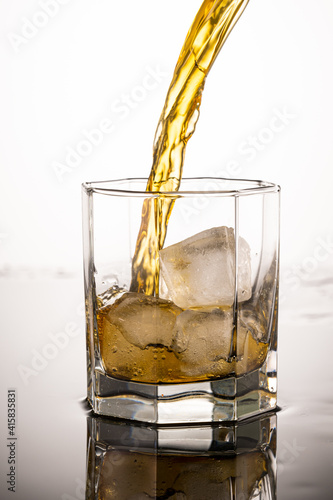 splash in glass with whiskey from falling ice on white background