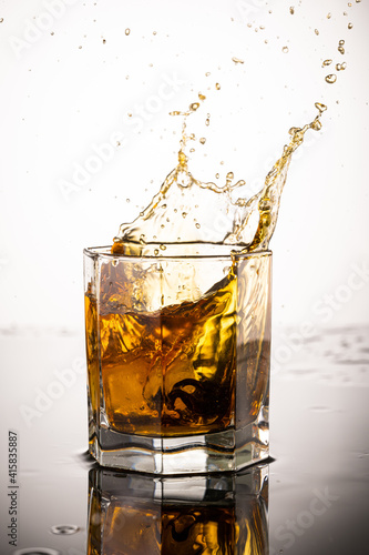 splash in glass with whiskey from falling ice on white background