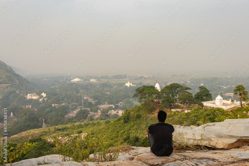 man sitting isolated at rock and watching amazing landscape