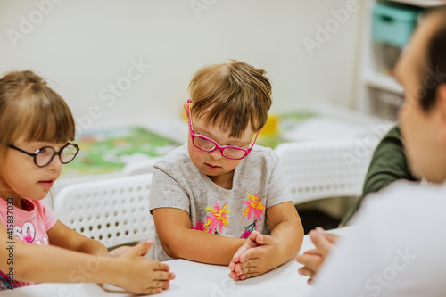 Young kids with down syndrome studying and playing in the room with white desks.