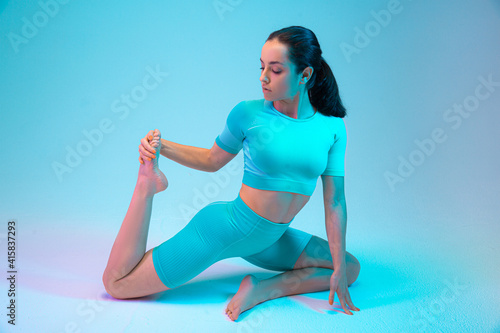 Portrait of young fit and sportive caucasian woman is stretching on gradient background. Brunette longhair model. Perfect body ready for summertime. Beauty, resort, sport concept. © Ivan