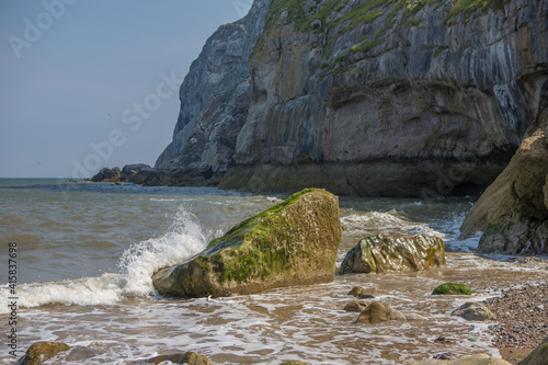 Wave splashing on the rocks at the base of the little Orme, Llandudno. North Wales pebble beach