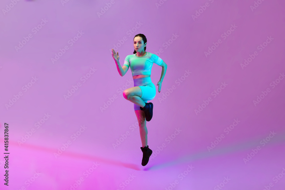 Young sportive woman training isolated on gradient studio background in neon light. athletic and graceful. Modern sport, action, motion, youth concept. Beautiful caucasian woman practicing.