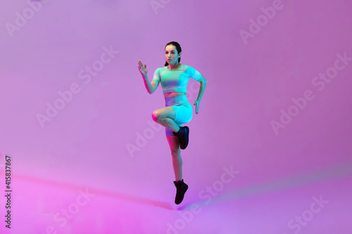 Young sportive woman training isolated on gradient studio background in neon light. athletic and graceful. Modern sport, action, motion, youth concept. Beautiful caucasian woman practicing.