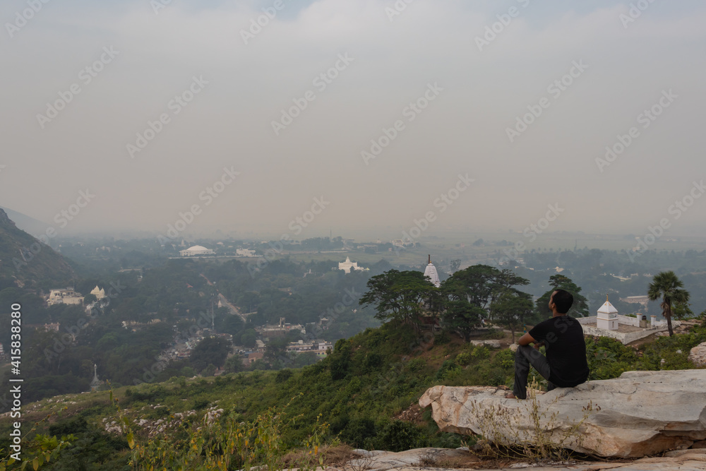 man sitting isolated at rock and watching amazing landscape