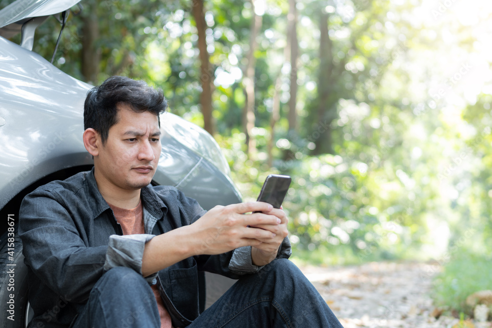 Man using phone for contact maintenance car service. Traveler sitting and using smartphone while Broken car. Man using phone for contact maintenance car service. Traveler sitting and using smartphone while Broken car.