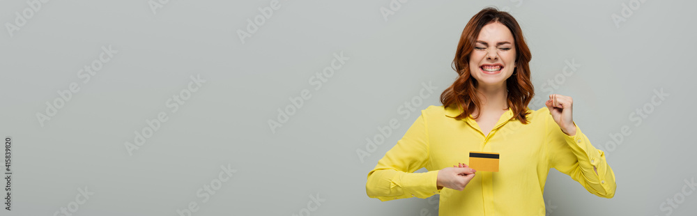 excited woman showing yes gesture while holding credit card on grey, banner excited woman showing yes gesture while holding credit card on grey, banner