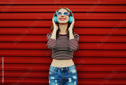 Portrait of happy young woman with wireless headphones listening to music on a red background