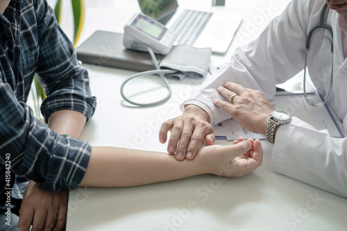 Close-up of a doctor examining the patient's pulse in the doctor office Medical device documents placed on the table.