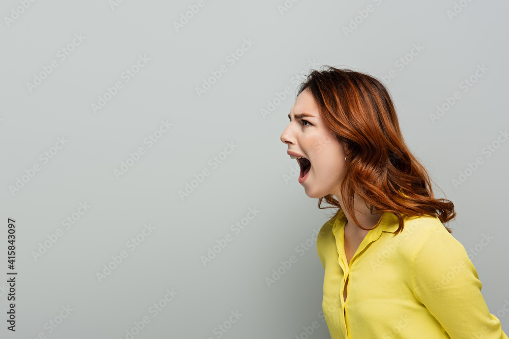 angry woman in yellow short screaming while looking away on grey angry woman in yellow short screaming while looking away on grey