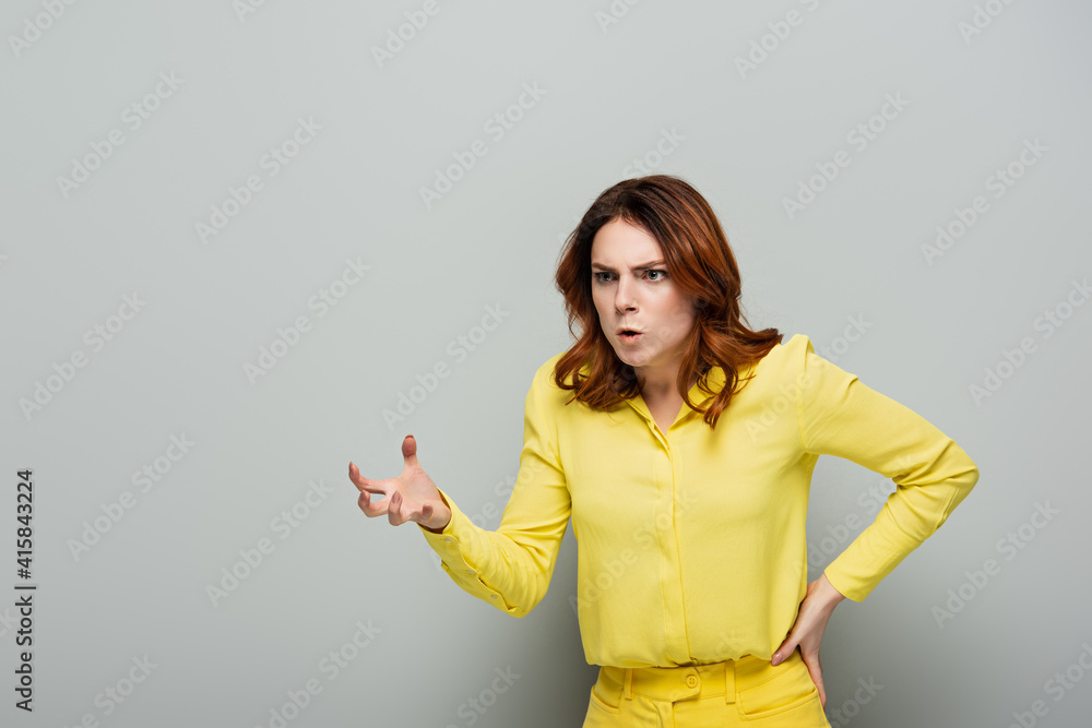 angry woman showing frightening gesture while standing with hand on hip on grey angry woman showing frightening gesture while standing with hand on hip on grey