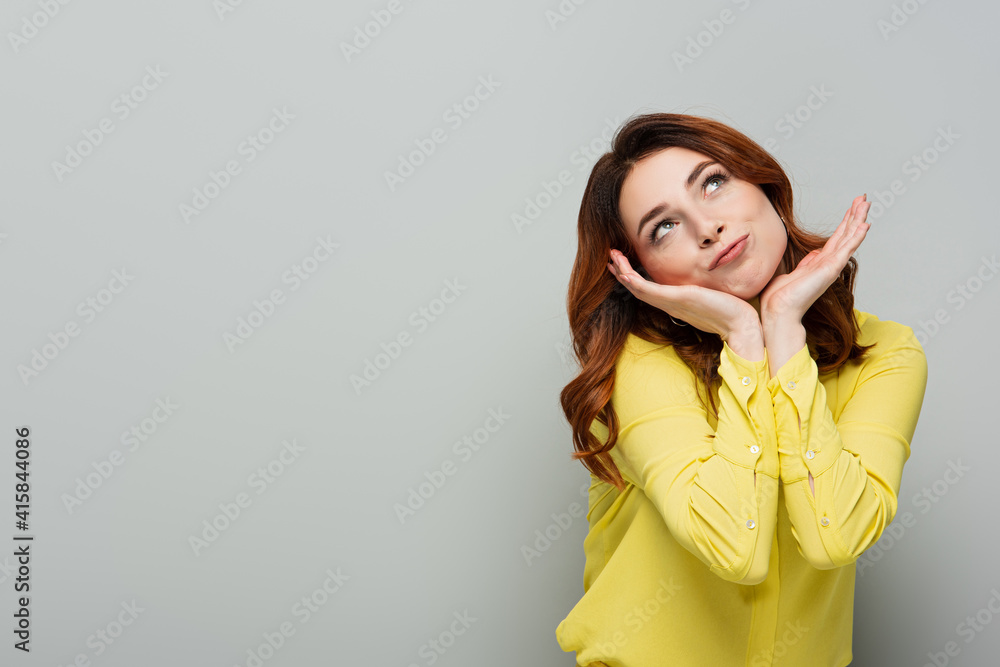 dreamy smiling woman looking up while holding hands near face on grey dreamy smiling woman looking up while holding hands near face on grey