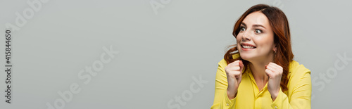 thrilled woman looking away while standing with clenched fists isolated on grey, banner