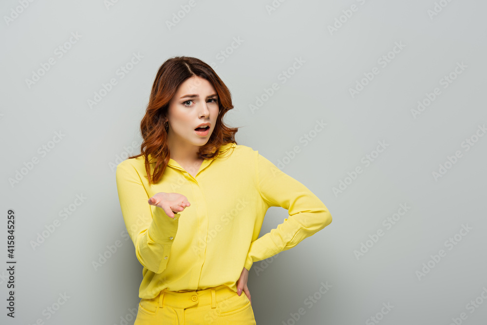 shocked woman pointing with hand while standing with hand on hip on grey shocked woman pointing with hand while standing with hand on hip on grey