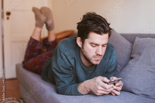 Serious man is lying on a couch with a smartphone 