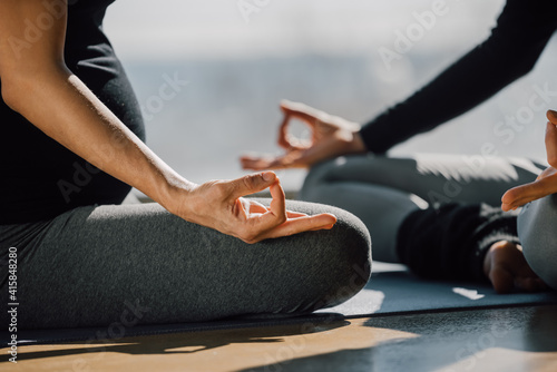 Close up of two woman sitting cross-legged in Padmasana  Lotus posture  yoga hands pose  focus on fingers in Jnana mudra. Pregnant woman in a prenatal yoga class. Unrecognizable people.