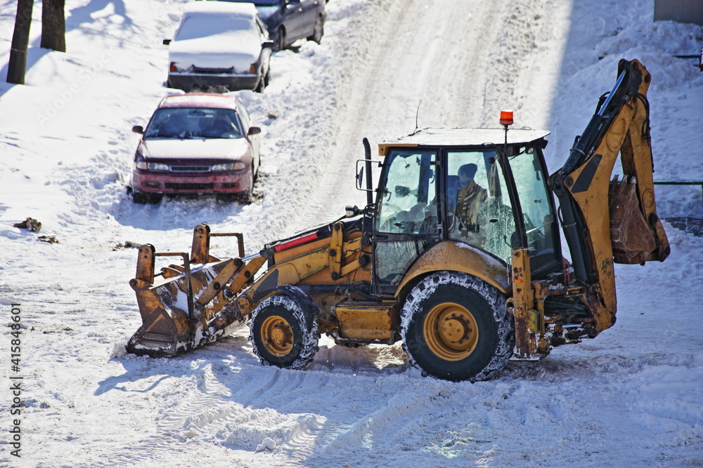 Yellow powerful wheeled bulldozer tractor removes a snow with scraper