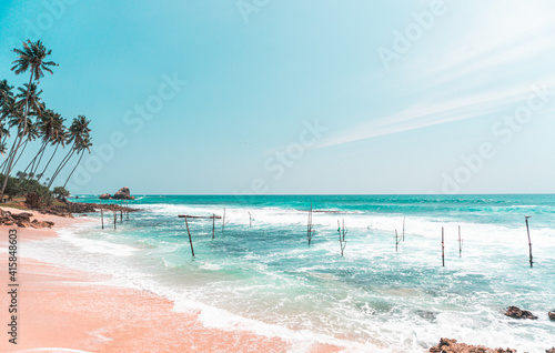 Fototapeta Naklejka Na Ścianę i Meble -  Tropikalna plaża z palmami, niebieski ocean z falami oraz kije rybackie.