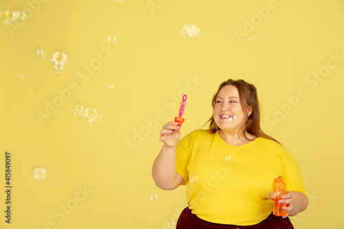 Soap bubbles. Beautiful plump caucasian plus size model isolated on yellow studio background. Concept of inclusion, human emotions, facial expression, sales, body positive. Copyspace for ad. © master1305