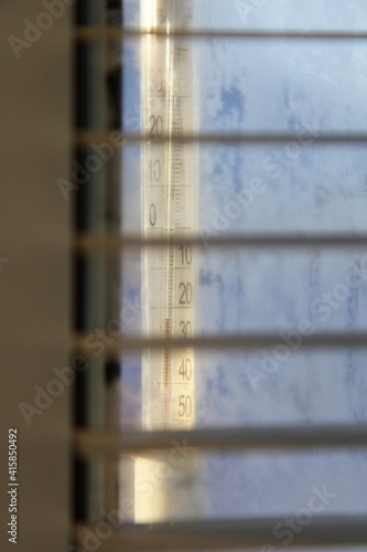 Outdoor glass mercury thermometer with temperature -23C cold on a frozen sunny winter day, closeup view through horizontal blinds, weather forecast illustration photo