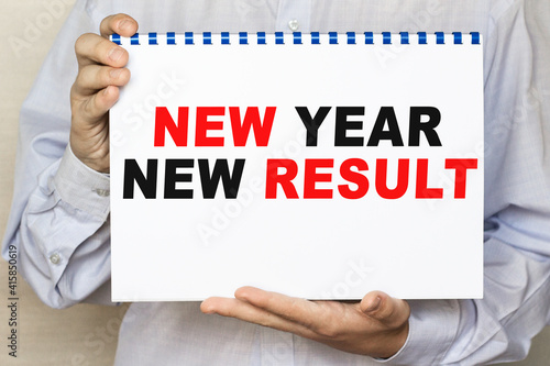 The businessman shows a sheet with the text NEW YEAR NEW RESULT on a white background. Business concept