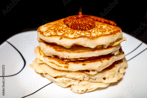 Syrup pouring onto a stack of fluffy pancakes against a black background.