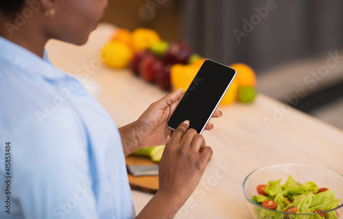 African Lady Using Phone With Empty Screen In Kitchen, Cropped