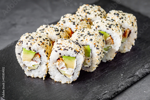 appetizing sushi roll california with eel avocado cucumber and sesame seeds on a black stone plate