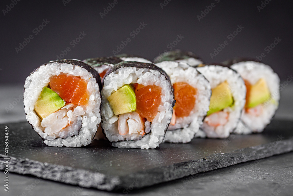 appetizing sushi roll futomaki salmon, shrimp and avocado on a black stone plate appetizing sushi roll futomaki salmon, shrimp and avocado on a black stone plate