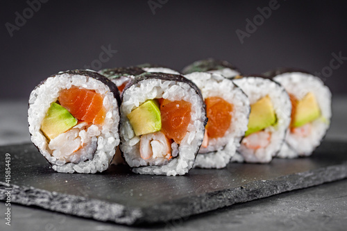 appetizing sushi roll futomaki salmon, shrimp and avocado on a black stone plate