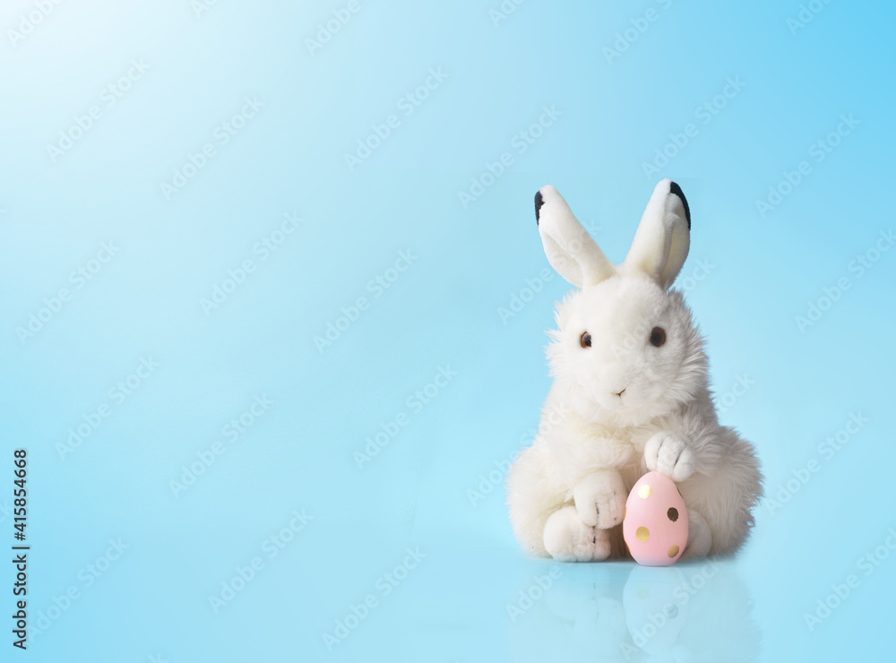 Fototapeta premium Easter bunny rabbit with pink painted egg on blue background. Easter holiday concept.
