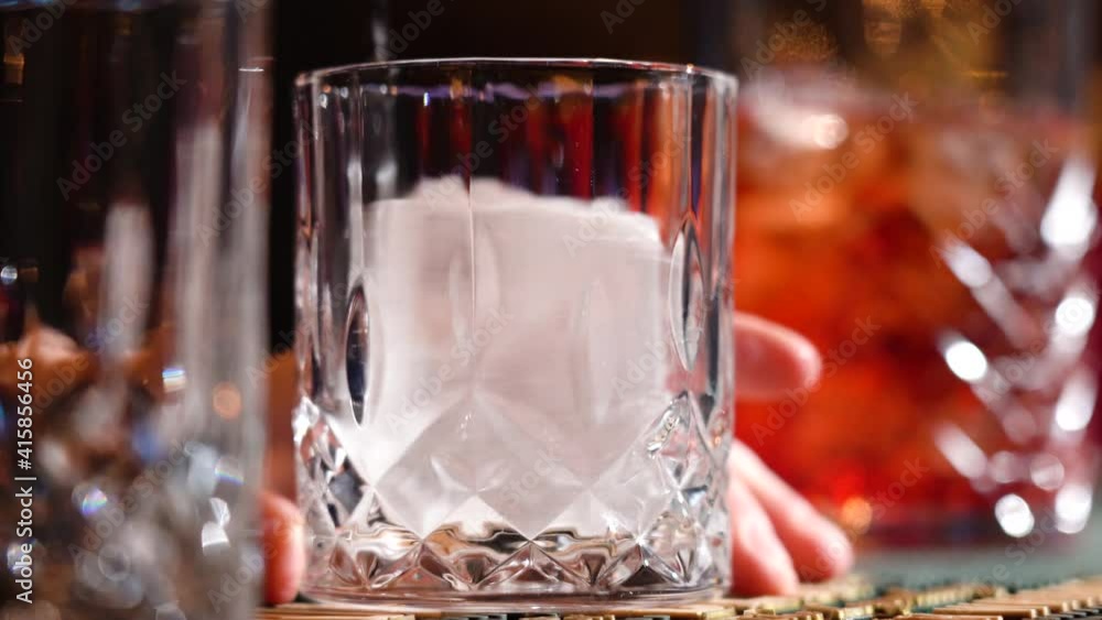 Close up bartender is putting professional crystal ice cubes in glass while preparing an alcoholic cocktail to customers bar or disco club. Close up bartender is putting professional crystal ice cubes in glass while preparing an alcoholic cocktail to customers bar or disco club.