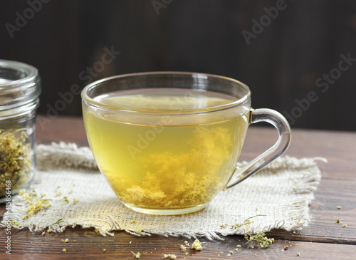 Meadowsweet floral herbal tea in glass cup with dried herb in a jar nearby on the wooden rustic table, closeup, copy space, natural medicine and healthy herbal tea concept